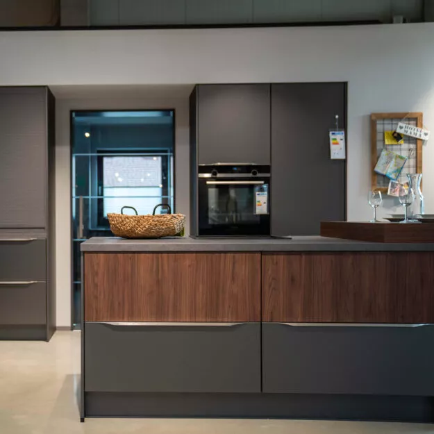 Moderne Küche mit Kochinsel und dunklen Wallnussfronten als Akzent in einer schwarzen Küche mit Kochinsel im Küchenstudio von Tischer & Teuber.