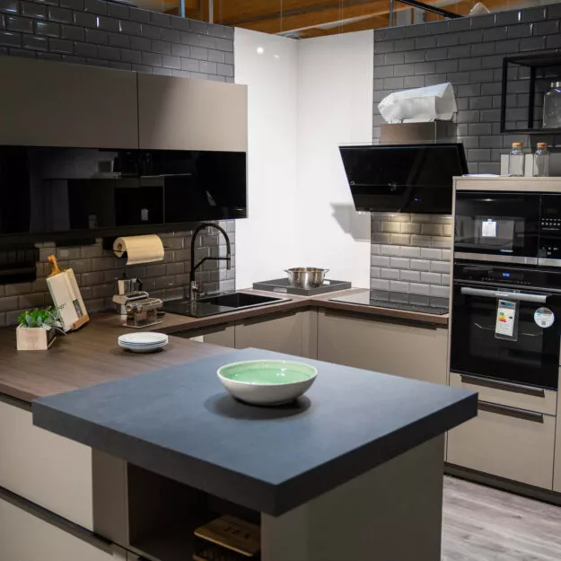 U-Küche in Mokka-beige mit dunkler Holzarbeitsplatte und modernen Einbaugeräten im Küchenstudio Tischer & Teuber.